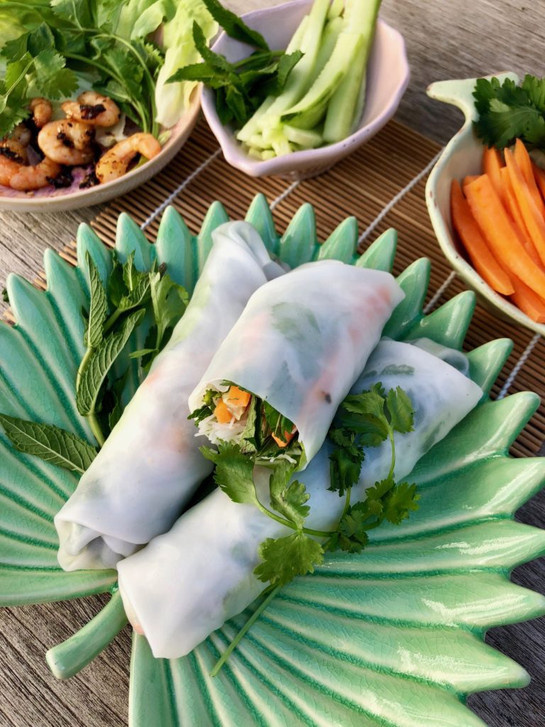 Summer rolls, a fresh delight! three rolls on palm plate with bowls close up
